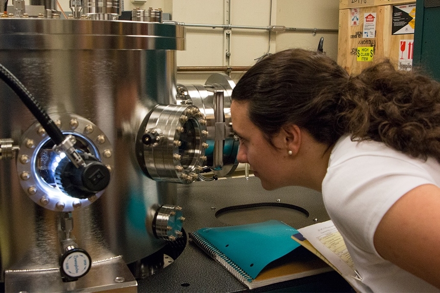 Summer Scholar Alexandra Oliveira looks inside a sputtering chamber used for building up atomically-thin layers of special magnetic materials such as manganese, gallium, and ruthenium. The machine is in the lab of Assistant Professor Luqiao Liu.  