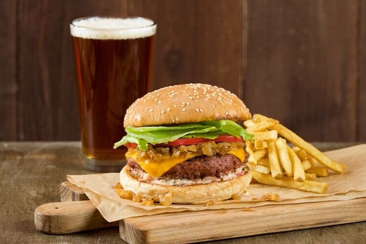 The Veggie Grill Beyond Burger includes a Burger by Beyond patty, vegan American cheese, grilled onions, house-made sauce, tomato, iceberg lettuce, and a sesame seed bun.