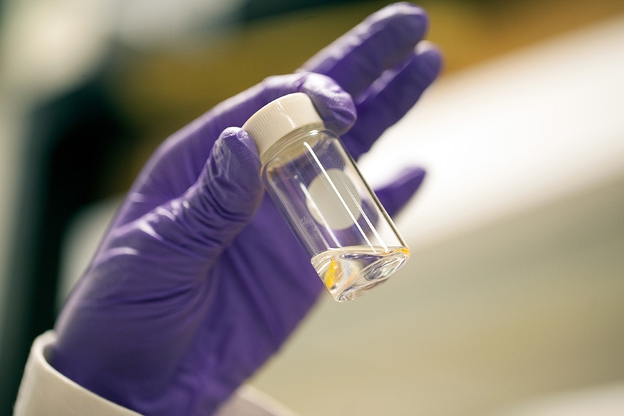 Graduate student Ingrid Guha holds a jar containing a clear liquid that looks like water to the naked eye, but it’s actually an emulsion of oil and water at the nanoscale. 
