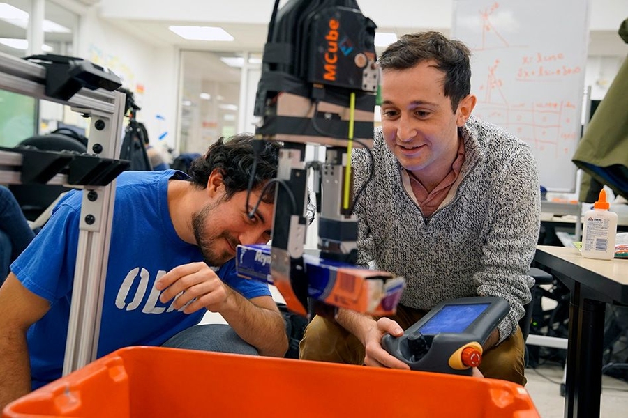 Elliott Donlon (left) and Francois Hogan (right) work with the robotic system that may one day lend a hand with this household chore, as well as assist in other picking and sorting tasks, from organizing products in a warehouse to clearing debris from a disaster zone. 
