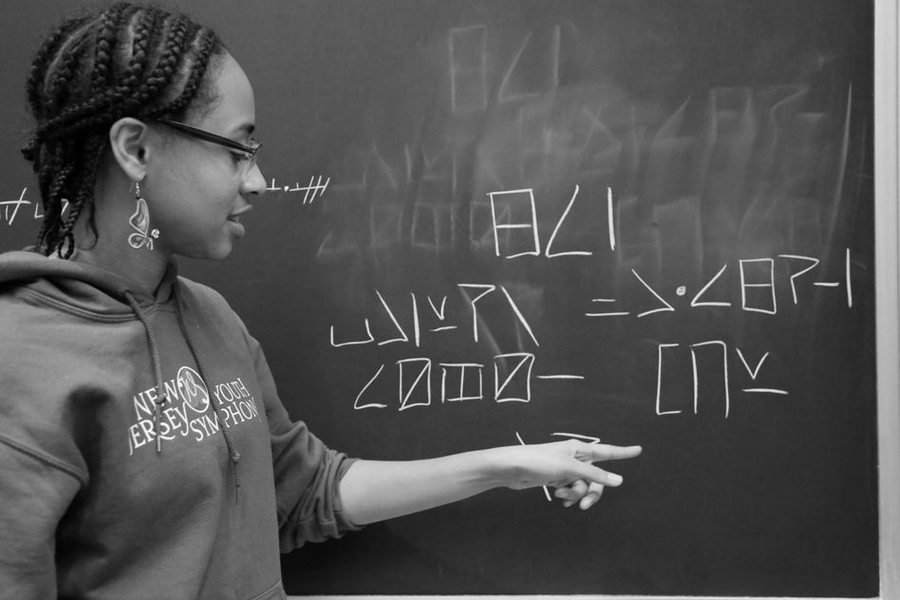 Junior Alyssa Wells-Lewis, with a written sample of "dænikjə," her constructed language. The sentence reads: "We know that she can write."