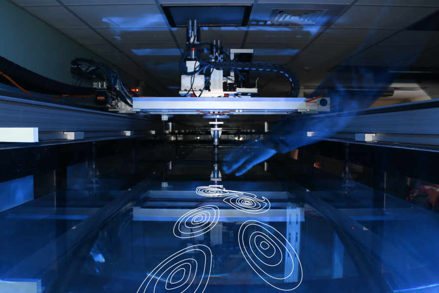 A researcher's hand hovers over the water's surface in the Intelligent Towing Tank (ITT), an automated experimental facility guided by active learning to explore vortex-induced vibrations (VIVs), revealing a path to accelerated scientific discovery.
