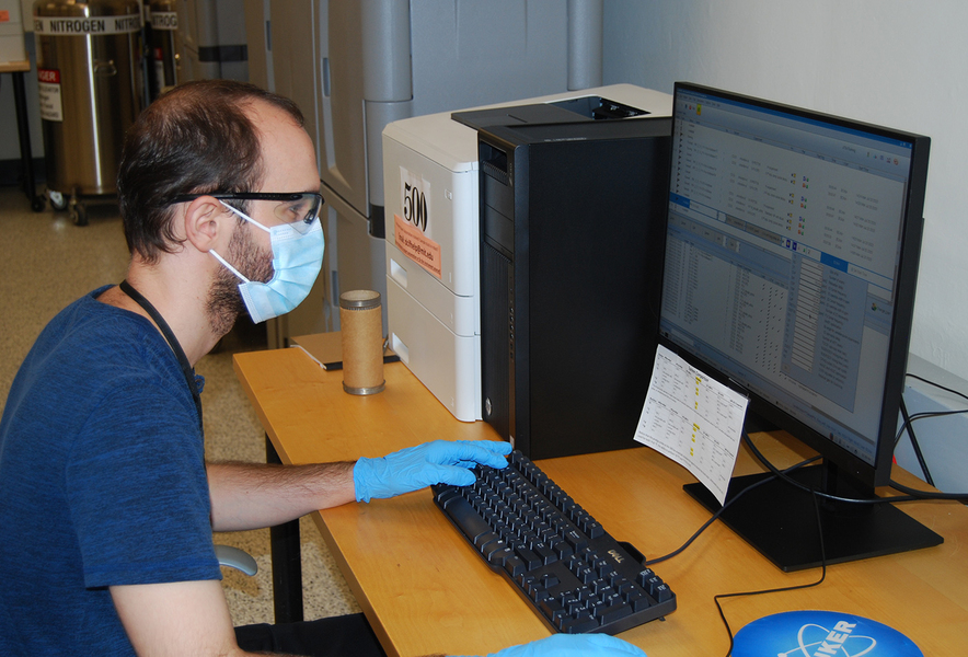 PhD student Ryan King sitting at an instrument wearing mask and gloves