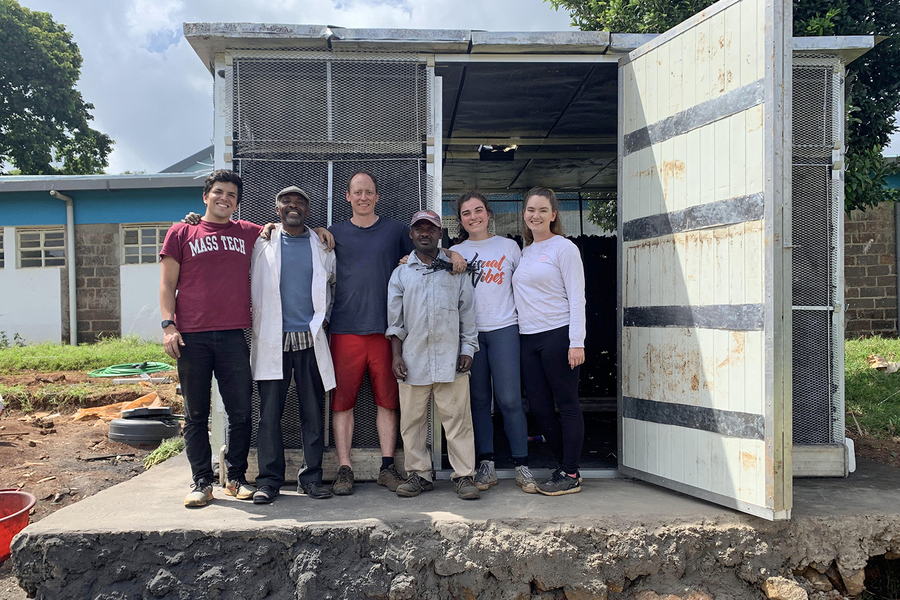 Six people pose in front of structure made of a shipping container