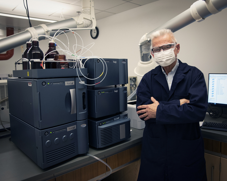 Photo of masked John Dolhun standing next to a new piece of lab equipement that looks like a stack of computers attached to bottles of liquid on top