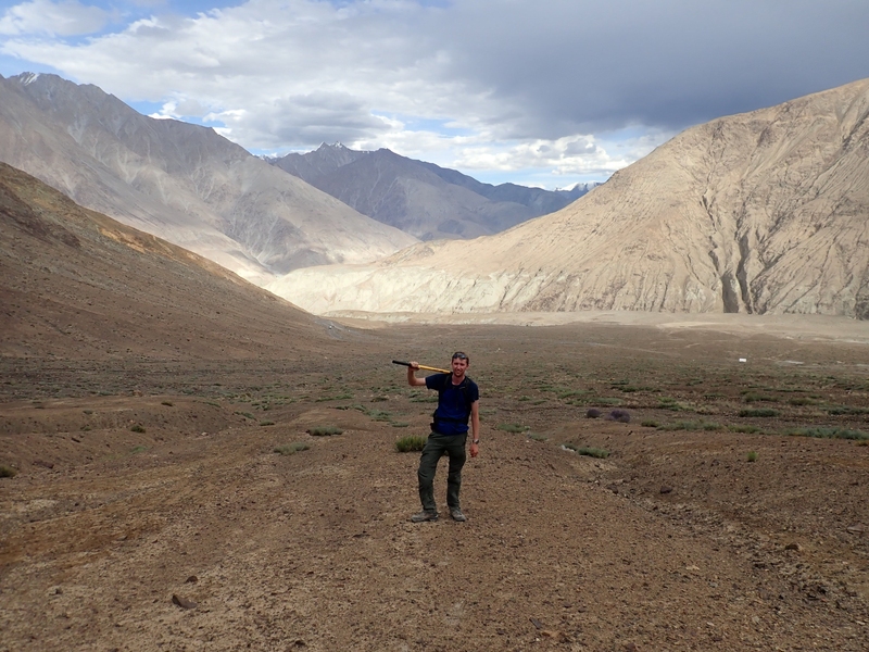 Photo of a man holding a pixaxe in the valley of a mountain range