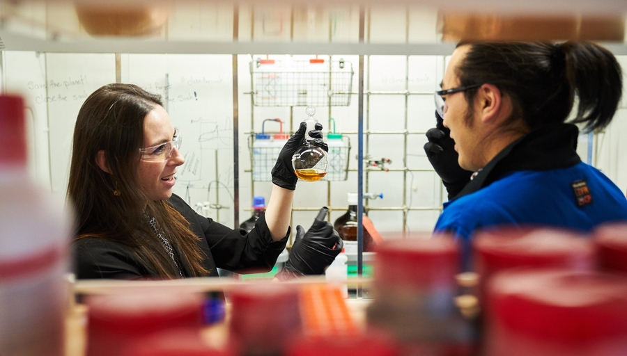 Photo of Julia Ortony with PhD student Yukio Cho, looking at a flask of yellow liquid