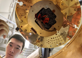 Photo of researcher Isaac Zheng in a lab next to a circular golden piece of equipment