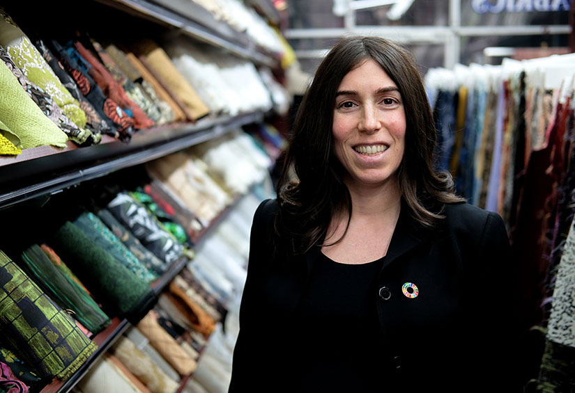 Photo of a Stephanie Benedetto surrounded by rows and racks of textiles