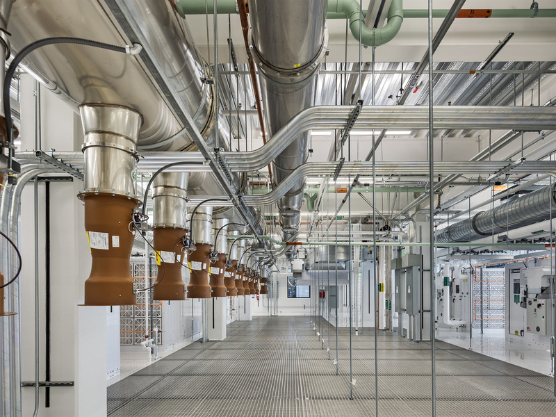 Photo of MIT.nano's fan deck, a brightly lit room packed with metal pipes of many sizes