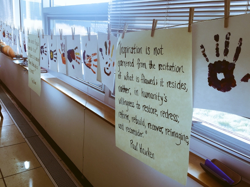 Photo of multicolored handprints hanging from a clothesline with an inspirational quote. 