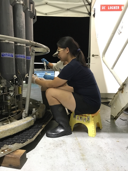 Photo of Tianyi Huang, seated and in profile, drawing seawater samples from an ocean CTD rosette.