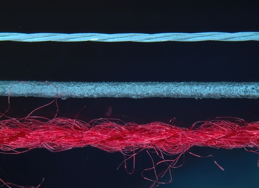 A highly magnified color image of three different textile fibers, one red, two blue.
