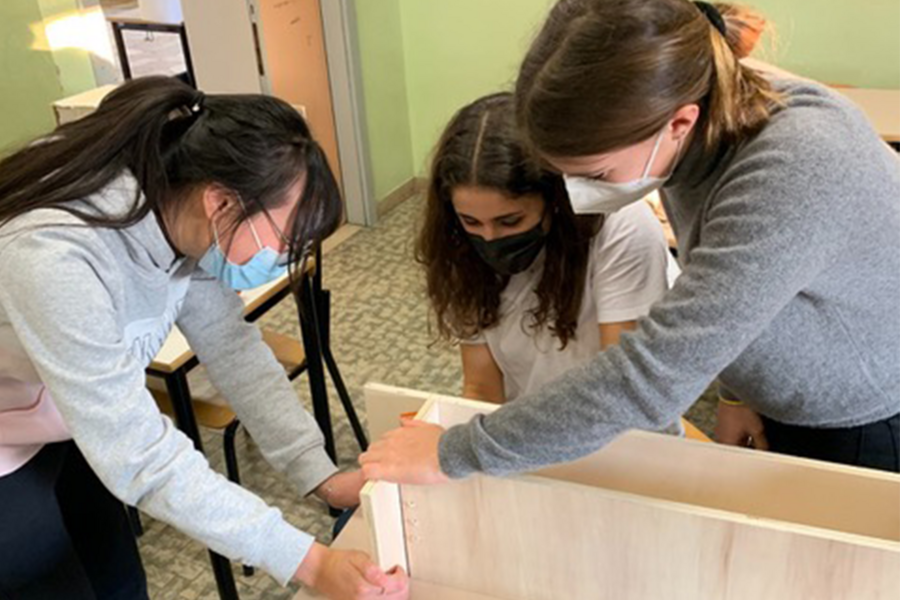 Photo of three students in a classroom working over a table-sized wooden structure