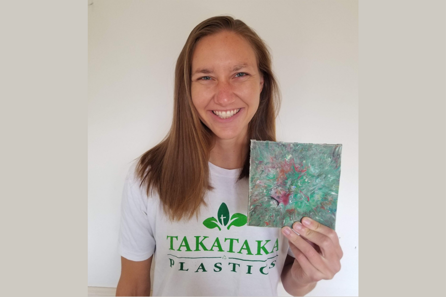 Photo of graduate student Paige Balcom wearing a Takataka Plastics T shirt, holding up a wall tile and smiling