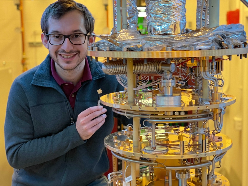 Photo of Daniel Rodan-Legrain standing next to a high-tech assemblage of tubes and disks