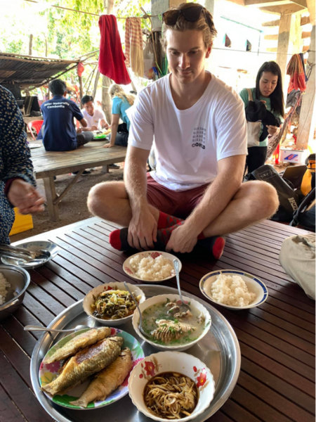Photo of Matthew Johnson sitting before several dinner plates filled with Cambodian food.