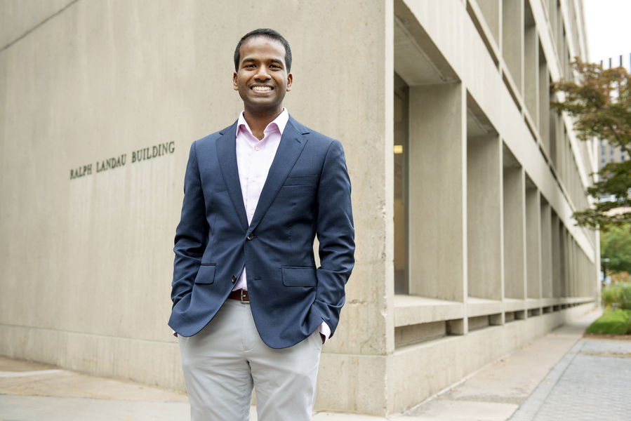 Karthish Manthiram profile photo. He is wearing a blazer and standing with his hands in his pockets in front of the Ralph Landau Building at MIT