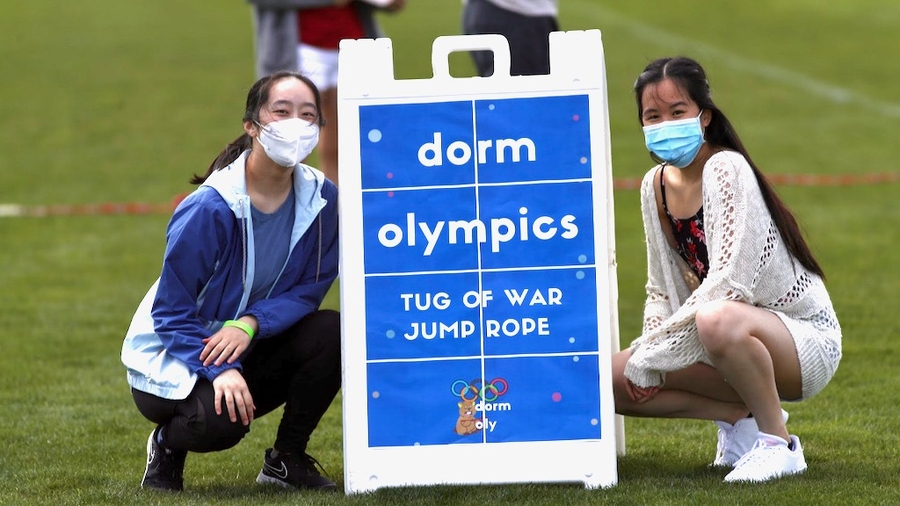 Photo of Ellie Feng and Ashley Ke crouching on either side of a sign that reads "Dorm Olympics: tug of war and jump rope"