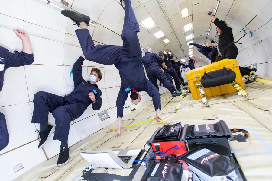 Photo of several people in blue jumpsuits experiencing microgravity in an aircraft interior