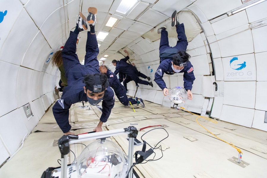 Photo of two people in blue jumpsuits and facemasks operating equipment in a microgravity environment