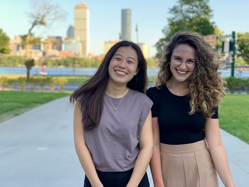 Photo of two young women standing outside in springtime, with the Charles River and the City of Boston as a backdrop