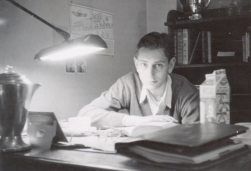 Black and white photo of a young Bob Logcher sitting at a desk with a lamp hovering over it