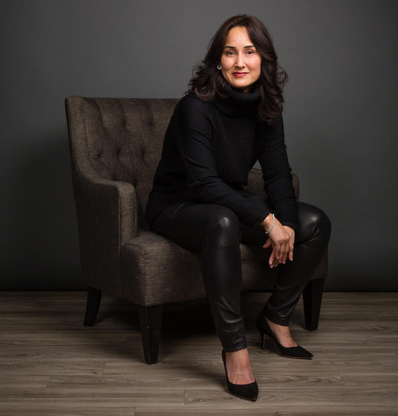 Portrait photo of Cynthia Breazeal, seated, wearing black clothes against a dark background