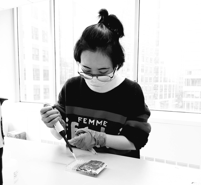 Black-and-white photo of Yining Hao working at her lab bench, pipetting liquid into a tray of wells.