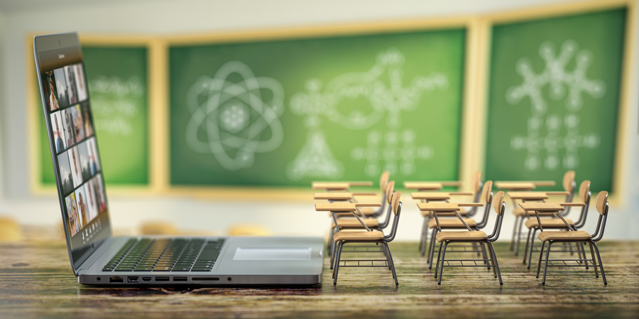 Photo of three rows of miniature desks in front of an open laptop, with blurred chalkboards in the background
