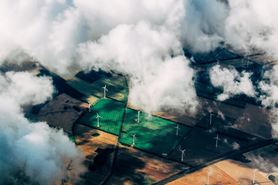 Aerial view of wind turbines across a field with clouds partially obscuring the view. 