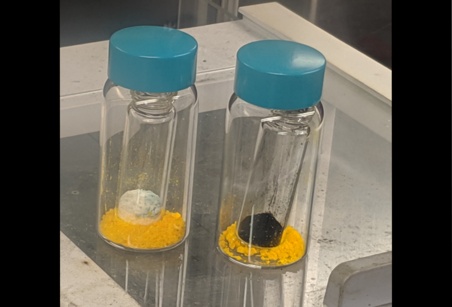 Photo of Two vials next to each other, one contains a white solid, the other contains dark solid. 