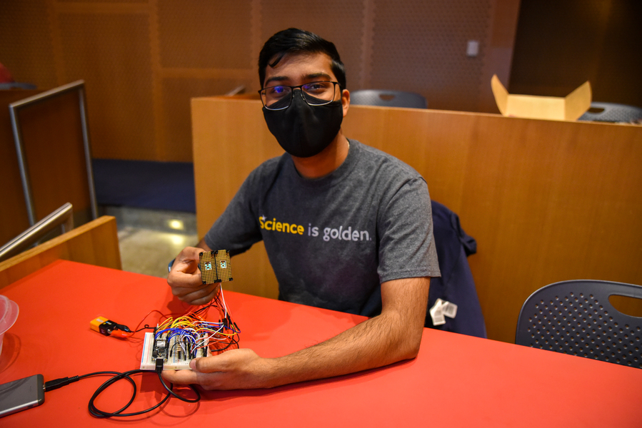 Photo of Syamantak Payra sitting at a workbench and handling electronics. 