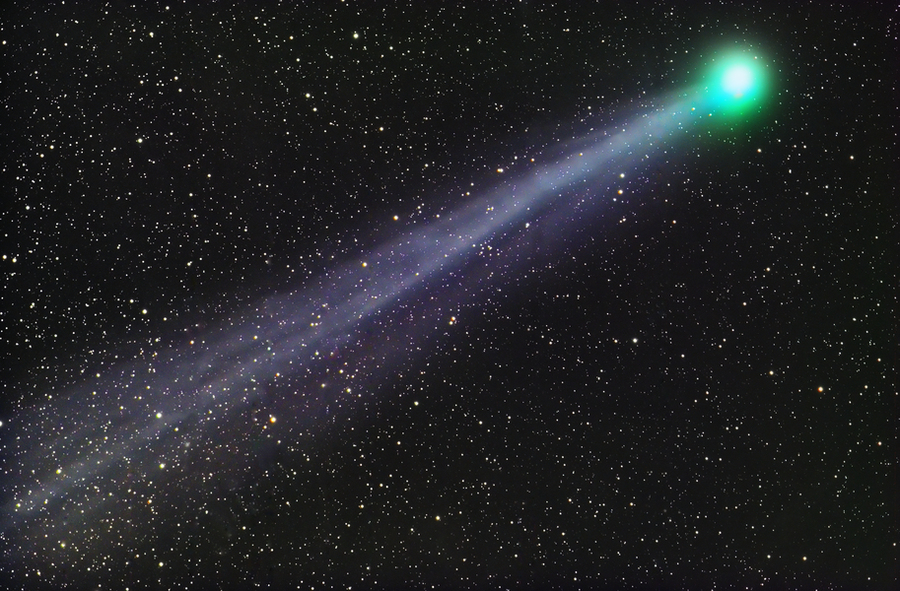 A comet with green coma travels from bottom left to top right, with a trail of light following