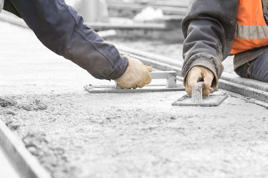 Photo of workers smoothing wet concrete. Close-up shows only their hands with trowels.