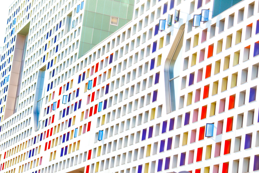 Photo of the face of MIT's Simmons Hall dorm, which is covered with small square windows, many of which have blue, red, and yellow colored panels on the side.