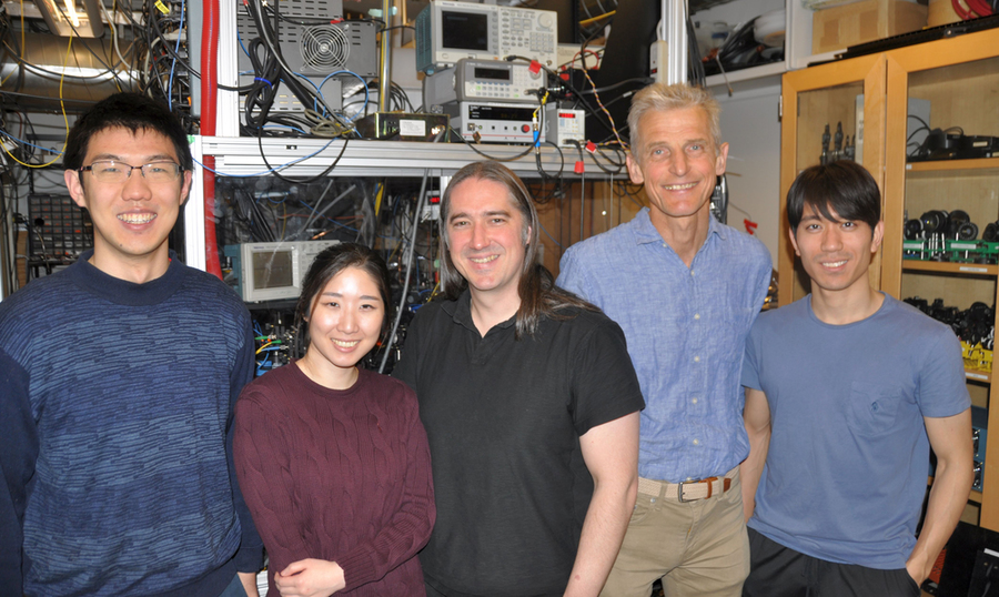 Photo of five people standing before racks of electronic equipment and smiling