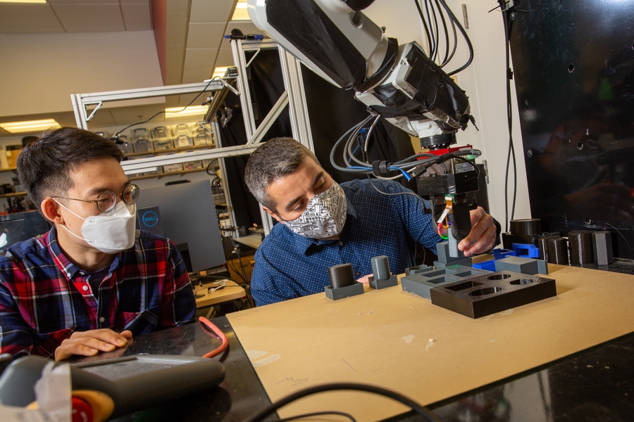 Photo of Professor Alberto Rodriguez and PhD student Sangwoon Kim, both masked, manipulating a robotic arm
