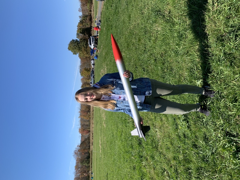 Photo of Summer Hoss holding a rocket in a green field under a blue sky