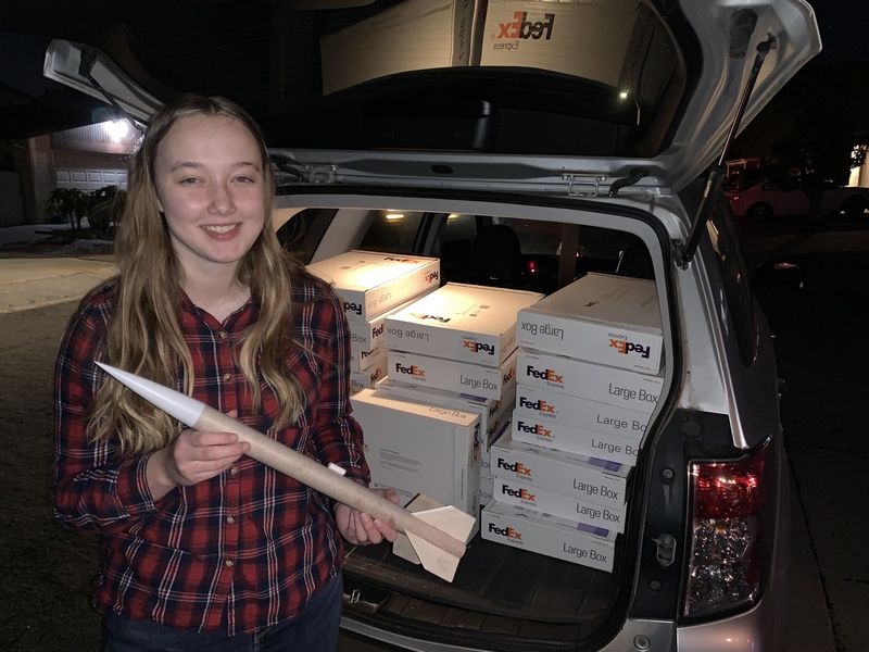 Photo of Summer Hoss holding a small rocket in front of a trunk packed with fedex boxes