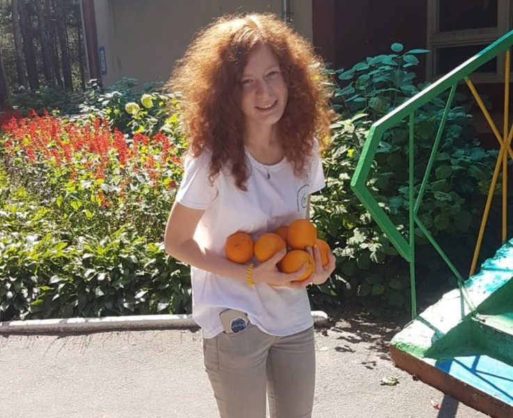 Photo of Yulia Zdanovska standing in front of a garden, holding oranges.