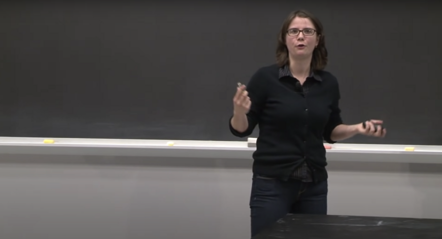 Lecturer Ana Bell gestures broadly while pacing in front of a blackboard.