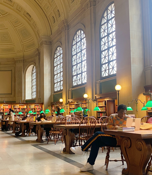 Photo of Milain Fayulu reading in a library with a high arched ceiling and windows