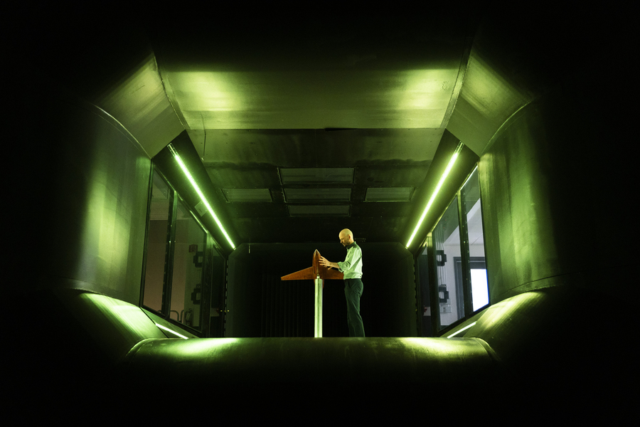 Photo of a man in a green-lit room adjusting a model airplane on a pylon