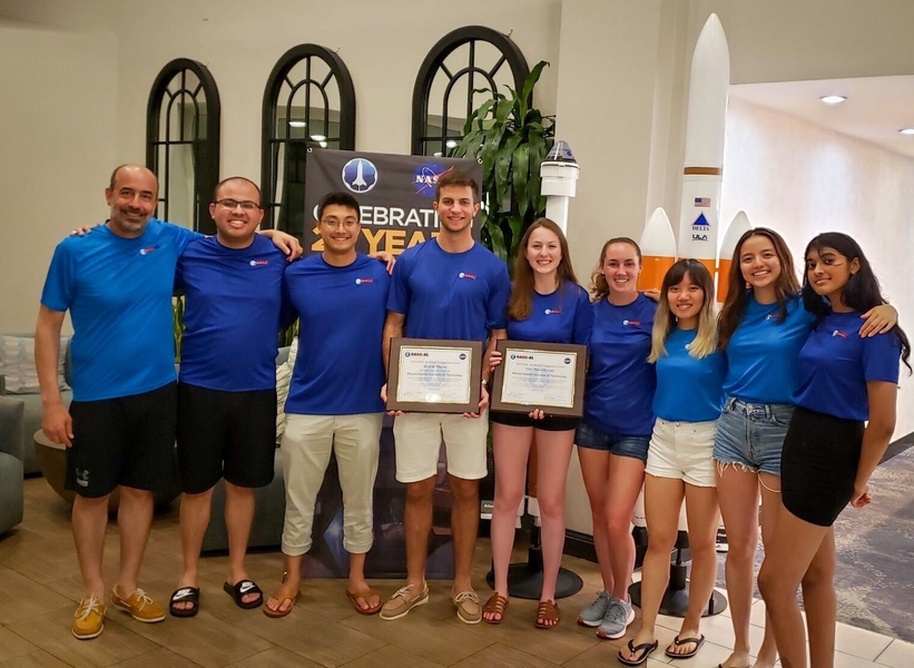 Photo of nine students, all wearing blue T-shirts, lined in a row, smiling, and holding certificate.