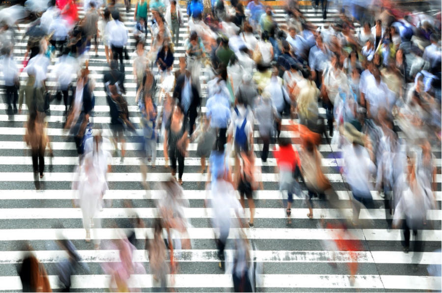 Photo of a crowd walking through crosswalk. The people are motion-blurred.