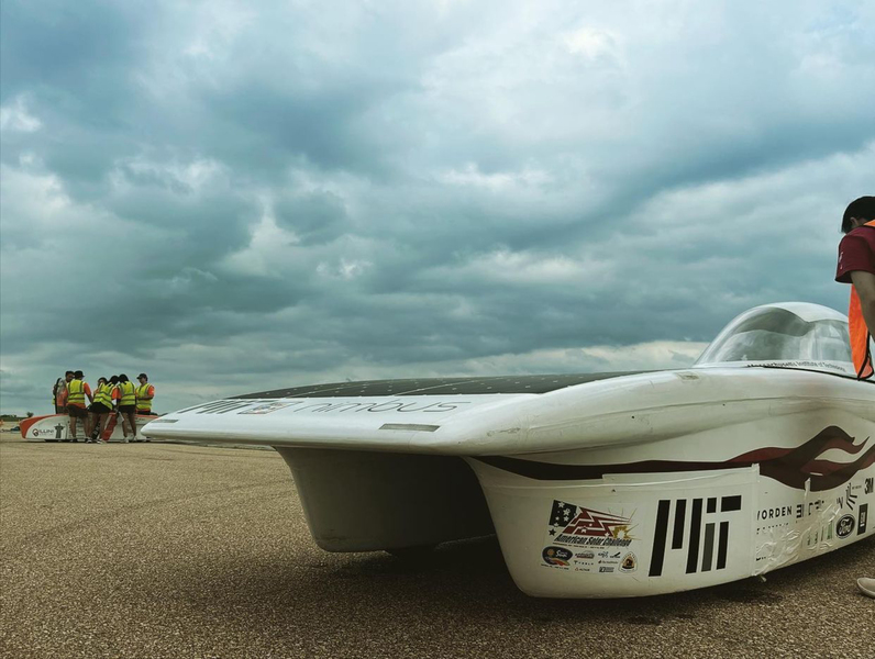 A photo taken at eye-level with Nimbus, against a cloudy sky, with another team and car in the background