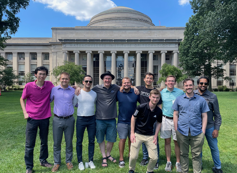 Group of 10 people posing on the grass in front of the MIT Dome