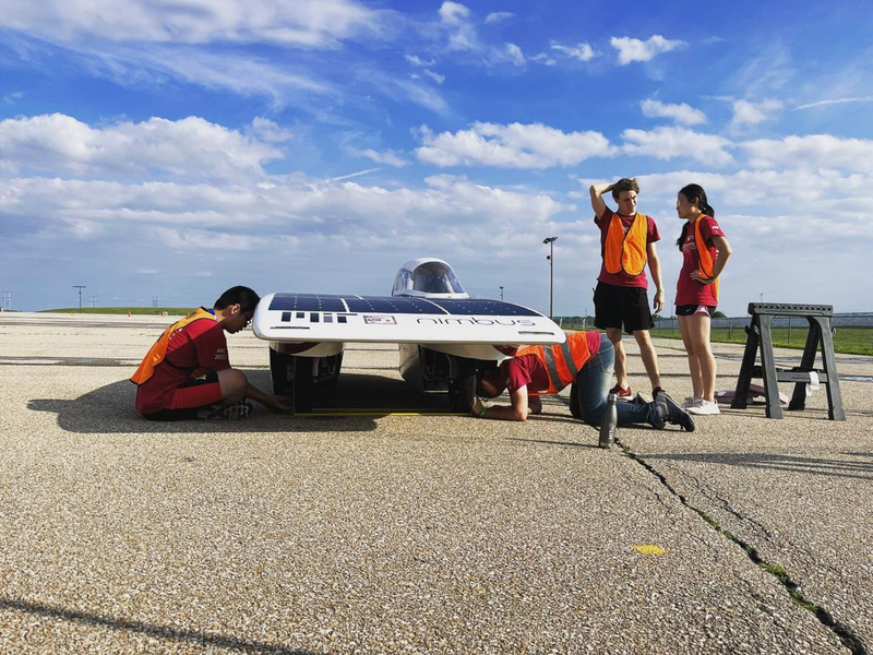 Two SEVT members work on car repairs while two others stand around at the American Solar Challenge