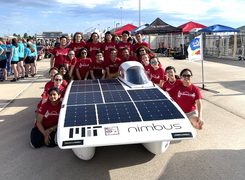 A team of 20 students crowds around the Nimbus solar car, wearing their red S.E.V.T. shirts